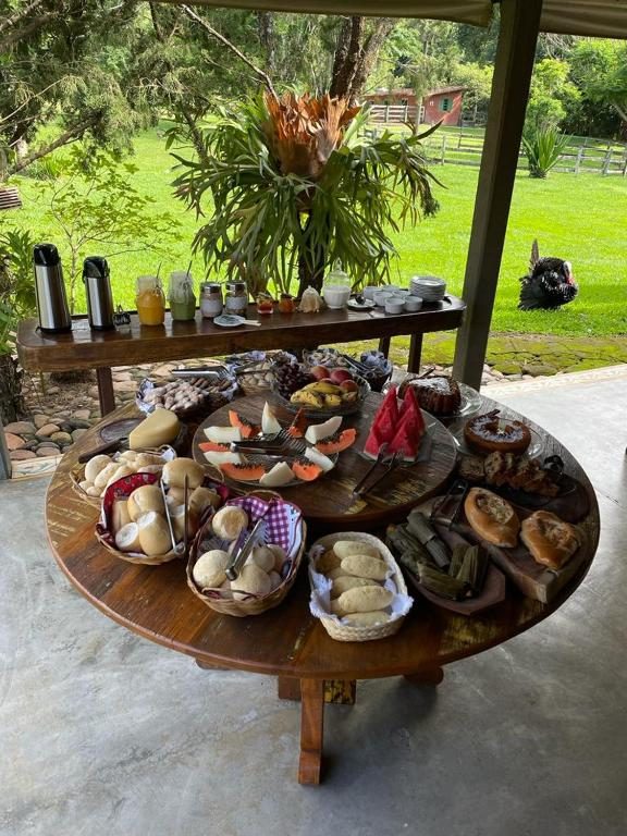 Mesa de café com queijo, pães, frutas e bolo, com o jardim ao fundo